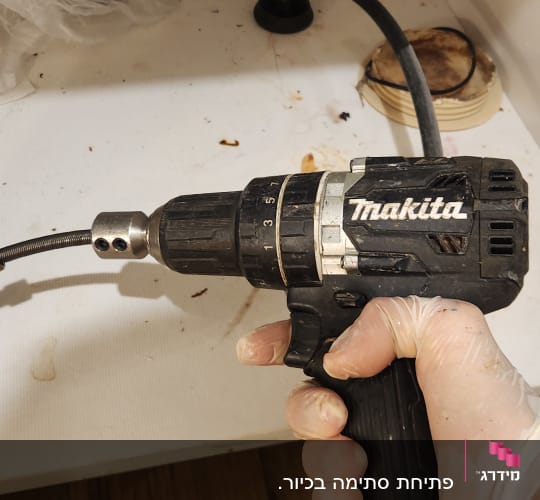 יד אוחזת במקדחה מתחת לכיור עם צינור